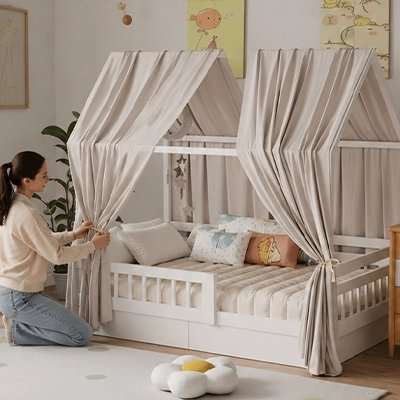 Ciel de lit cabane en bois clair avec toit en tissu rayé beige, rideaux amovibles et couchette enfant décorée de coussins colorés