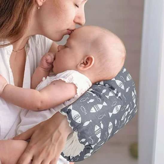 Coussin d’allaitement ergonomique gris en tissu à motifs de poissons blancs, en arc autour du bras pour soutenir bébé.