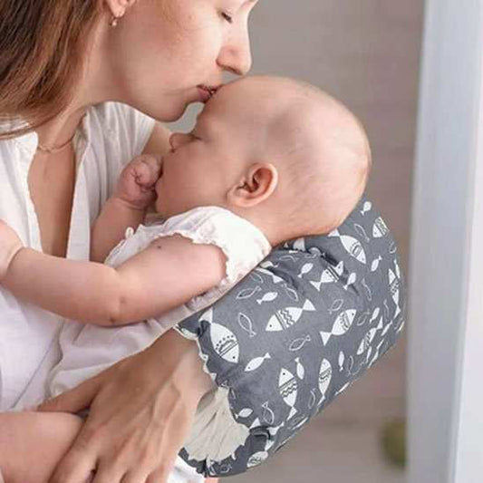 Coussin d’allaitement ergonomique gris en tissu à motifs de poissons blancs, en arc autour du bras pour soutenir bébé.