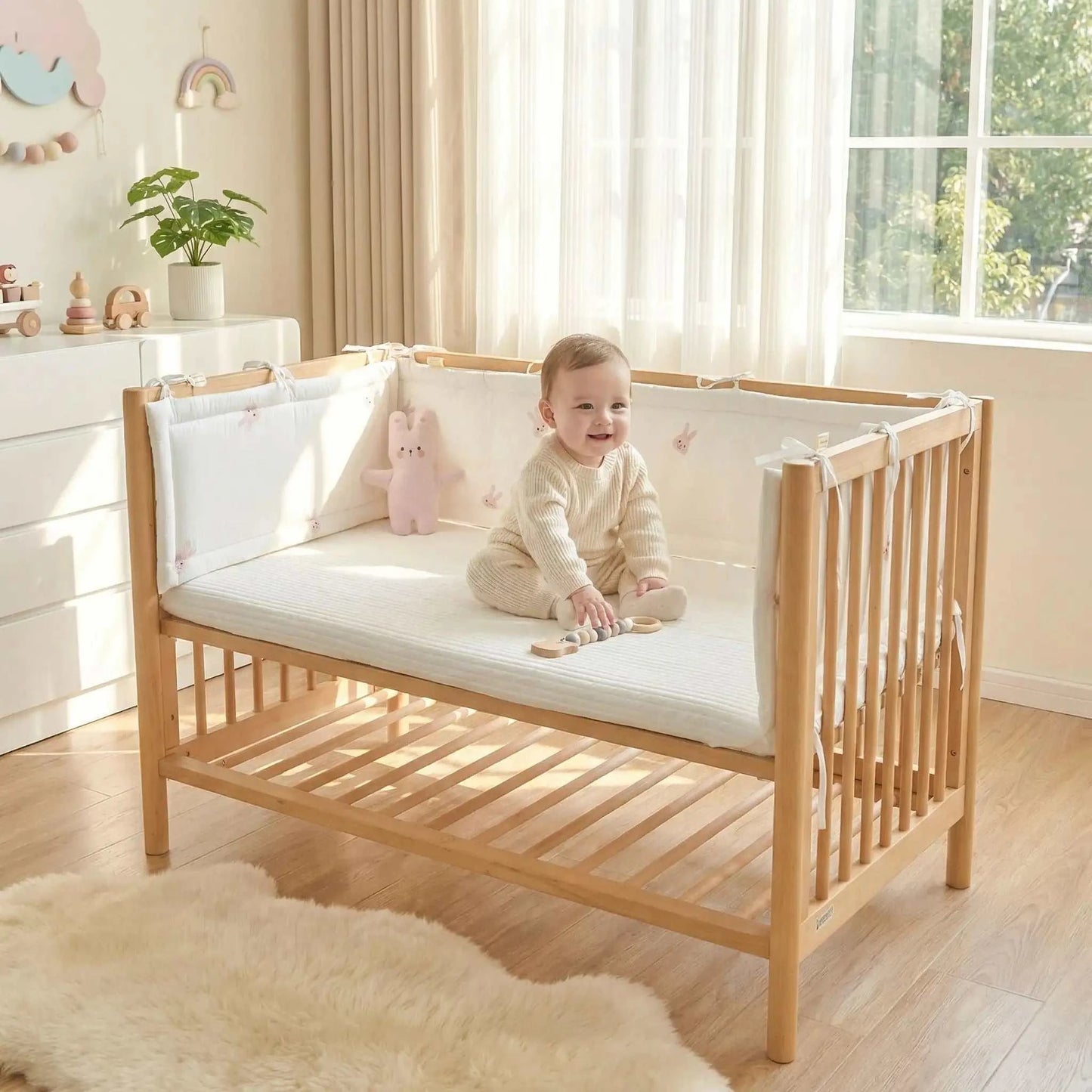 bébé assis sur son lit protéger par un tour de lit bebe motif lapin rose